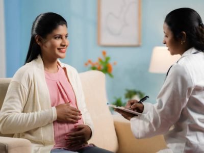 Indian doctor or nurse counseling pregnant woman at home by writing report at home - concept of home health checkup, maternity assistance and Medicare support